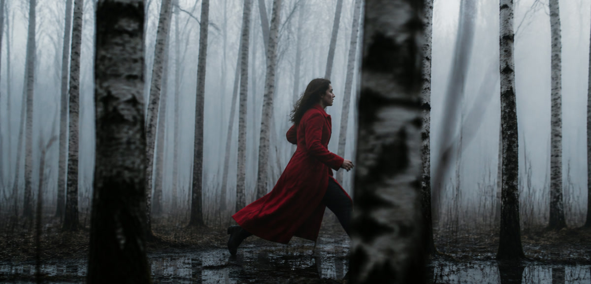 Woman in a scarlet coat running between birch trees through low fog